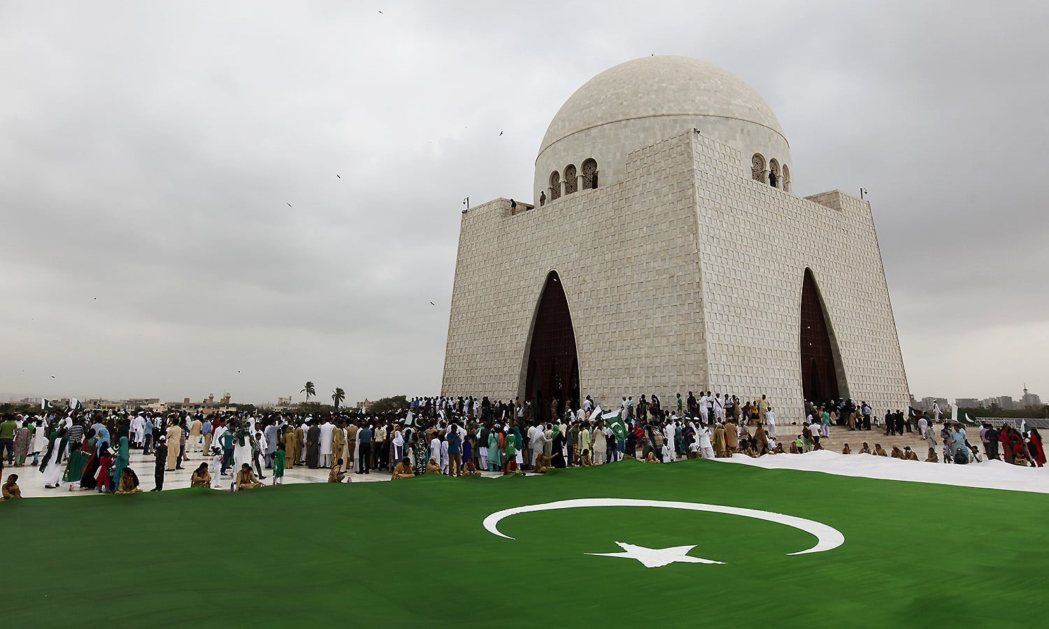 People gather near a national flag during a ceremony to celebrate the country's 69th Independence Day at the mausoleum of Muhammad Ali Jinnah in Karachi, Pakistan, August 14, 2015. Jinnah is generally regarded as the founder of Pakistan. REUTERS/Akhtar Soomro